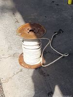 Full view of a large spool of white insulated house wire on a rusted metal spool, lying on concrete ground with shadows.