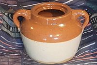 Photo of a two-tone glazed bean crock with two handles, brown glaze upper half and cream glaze lower half, showing the overall condition and shape.