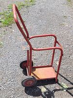 Side view showing red metal welding cart with base platform and handlebar. Two different sized wheels visible.