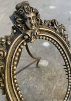 Close-up of the upper front of the metal frame showing the detailed female bust and floral decorations