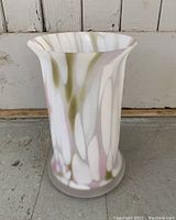 Vintage large white frosted Murano-style glass vase with splattered white, green, and pink design placed on a tile floor in front of a rustic wood wall.