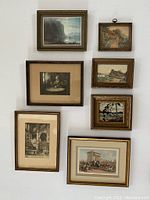 Photo of seven small antique framed artworks hung on white wall.