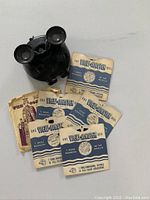 Photo showing the black View-Master stereoscope viewer with seven paper reels spread beside it, including coronation and England scenes.