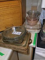 Glass pie plates and baking pans stacked on wicker tray and countertop near stove, showing condition and items included.