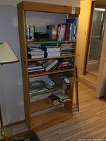 Full view of solid pine bookshelf filled with books and some boxes, showing five adjustable shelves and natural wood finish.