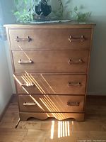 Front view of the dresser showing four drawers with wooden handles, medium wood finish, and a curved base edge detail. Plant on top is excluded.