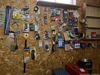 Wall-mounted assortment of hardware items including brushes, drill bits, door hardware, fasteners and tapes.