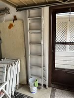 View of both aluminum ladders standing upright near a door, showing their relative heights and condition.