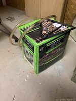 Closed box of Moisture Master Landscape Drip Watering System with poly-hose laying on top, placed on concrete floor.