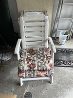 Frontal view of one white plastic lawn chair with floral seat pad, five chairs stacked behind.