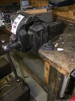 Side angle view of the vise mounted on wooden workbench showing handle and body with some surface wear.