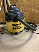 Front view of Shop Vac showing brand, wet/dry label, hose connected, and caster wheel underneath.
