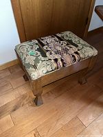 Wood footstool with patterned fabric upholstered top showing side angle on wood floor