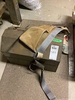 Metal toolbox on floor with suede tool belt on top showing wear and rust