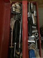 Top view of metal toolbox showing screwdrivers, wrenches and socket bits neatly arranged in compartments.