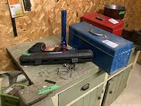 Overview of green workbench with blue and red metal toolboxes, flashlight, and various hand tools.