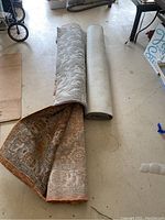 View of two rolled area rugs side by side, one with visible traditional pattern edge.