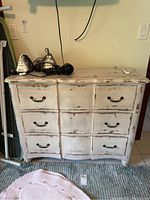 Front view of the distressed cream/white painted wooden dresser showing three drawers with black metal handles and wear marks.