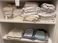 Shelves with stacks of folded bed sheets and pillowcases in various neutral tones and patterns