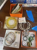 Overview of bracelets, earrings, rings in boxes on table with books in background.