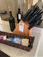 Overall kitchen counter showing olive oil bottle, knife block with knives, and woven basket with tea packets.