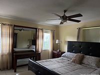 Curtains and rods mounted in bedroom windows showing beige fabric and sheer drapes, wood furniture visible in background.