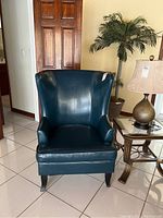 Front view of teal faux leather wingback chair with dark wooden legs, showing the high back and seat cushion.