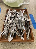 Overhead view of assorted stainless steel flatware and cutlery in a wooden tray on countertop.