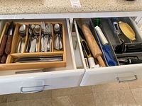 Two adjacent kitchen drawers open showing assorted flatware and kitchen utensils organized inside.