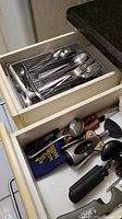 Overview of two kitchen drawers showing Cambridge stainless steel flatware set in top drawer and assorted kitchen tools in bottom drawer.
