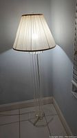 Full view of the floor lamp showing the cream pleated lampshade and the tall lucite rod base in a corner of a room.