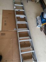 Full length view of aluminum extension ladder placed on cardboard flooring.
