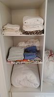Shelves with mixed linens including white folded sheets, gray towel, blue towels stacked, and patterned animal print fabric.