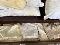White pillowcases with piping on a dark wooden bed frame with folded linens beneath.