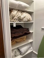 Shelving unit containing folded blankets, a folded comforter with palm tree pattern, and a white pillow on top.