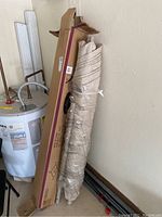 Patio umbrella wrapped in plastic next to cardboard packaging and water heater.