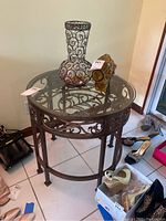 Front view of the round glass top side table with metal scrollwork and items on top.