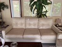 Front view of beige faux leather sofa with removable seat cushions and tufted back cushions.