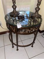 Side angle view of round glass top coffee table showing ornate metal base and glass top with two decorative item bases on top.