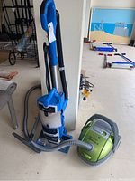 Blue Shark upright vacuum and green Electrolux canister vacuum shown side by side on floor