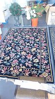 Full view of the black floral area rug with floral pattern and overlocked edges.