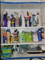 Wide view of cleaning supplies on two shelves showing a variety of spray bottles, aerosol cans, a box of Swiffer Sweeper dry cloth refills, and a container of wipes.