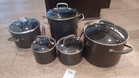 Full set of 5 Anolon cookware pieces with lids on display on floor.