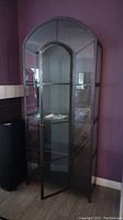 Front angled view of the glass fronted curio cabinet showing door partially open, glass shelves and arched top glass panel.