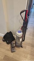 Full view of upright vacuum with wand, motorized head and black carrying bag (background)