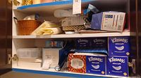 Photo showing shelving with multiple boxes of Kleenex Ultra Soft tissues, baskets and bags of latex gloves and masks.