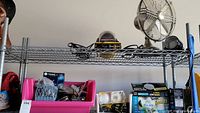 Wide shot of vintage Hunter fan, various lighting boxes, car vacuum, Rust-Oleum paint, and small items organized on metal shelving unit