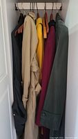 All five coats on a wardrobe rail: black, beige, yellow, magenta and dark green.