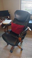 Front angle view of black La-Z-Boy office chair with red pillow, showing cushioned seat and wooden armrests with caster wheels on floor.