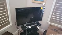 42 inch LG flat screen TV sitting on a black metal and glass stand next to a window with some cardboard boxes nearby.